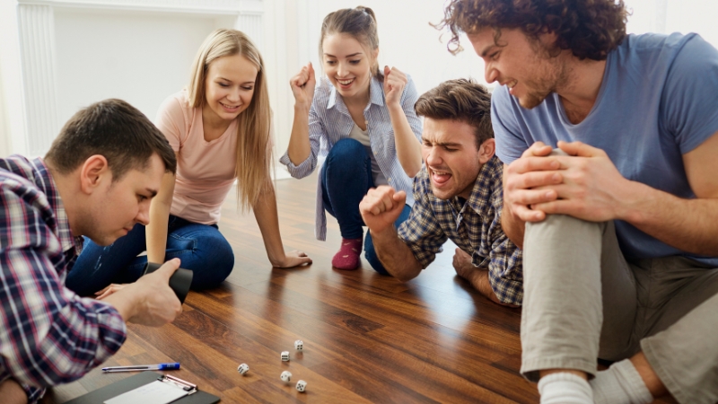 Students sit in a circle on the floor, excitedly playing a dice-based board game together