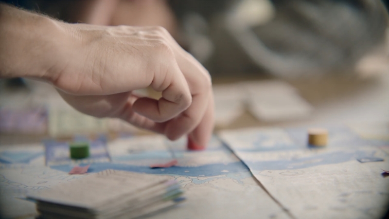 A person moves a game piece on a detailed board during a group board game session