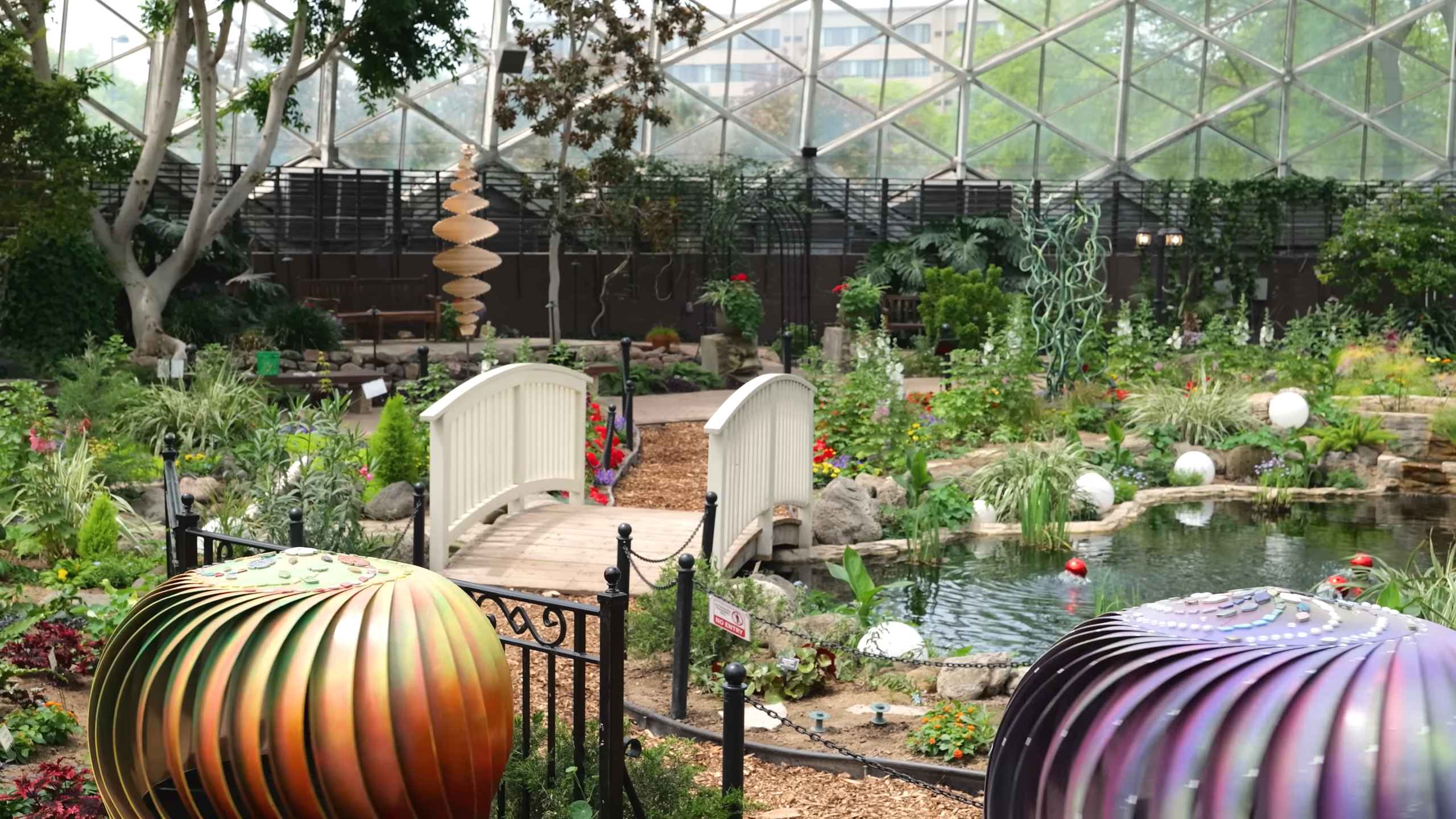 Interior of the Mitchell Park Domes in Milwaukee showing lush plants, a small bridge, pond, garden sculptures, and geometric glass architecture