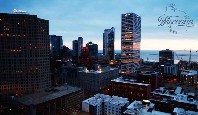 Cityscape of downtown Milwaukee, Wisconsin, at dusk showing tall modern buildings, including the US Bank Center, with Lake Michigan visible in the background