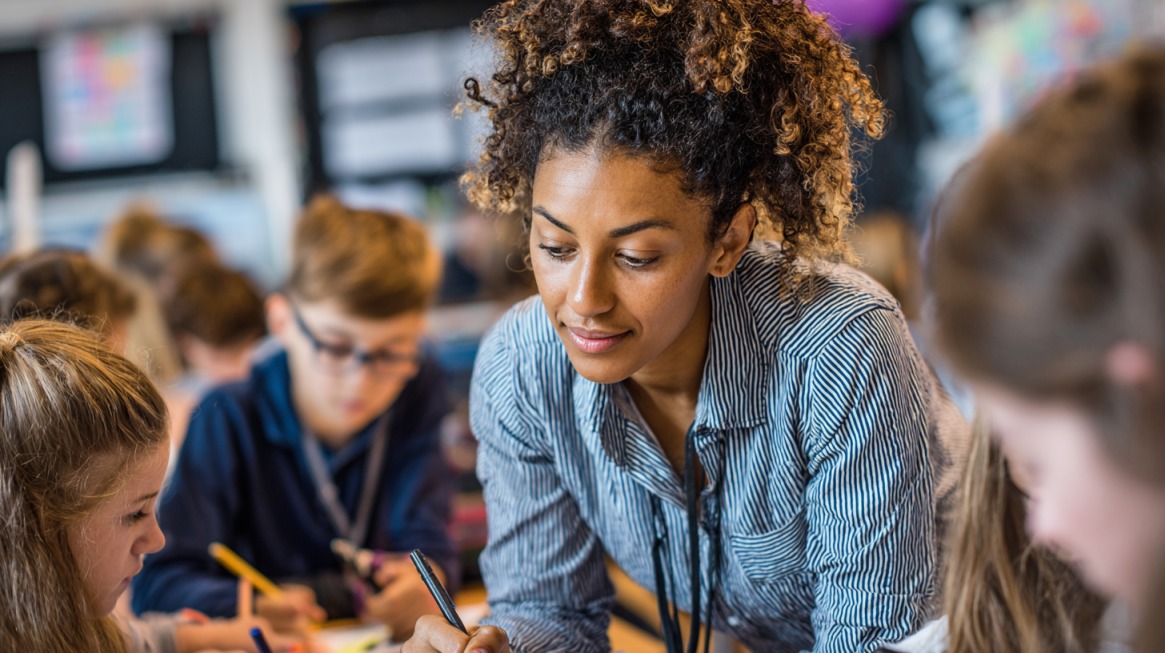 Teacher working closely with students at a table while reviewing their work