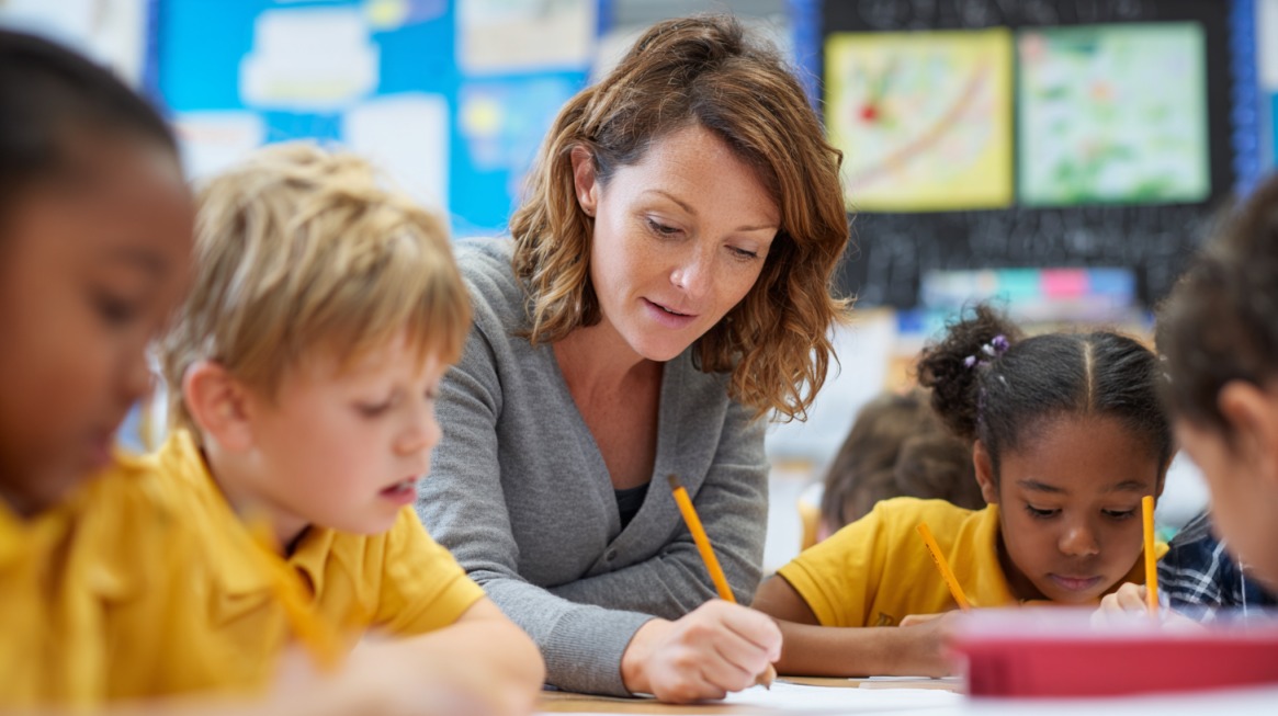 Teacher assisting young students with writing activities in a classroom