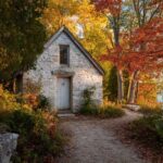 Small stone cottage surrounded by colorful autumn trees beside a lakeshore