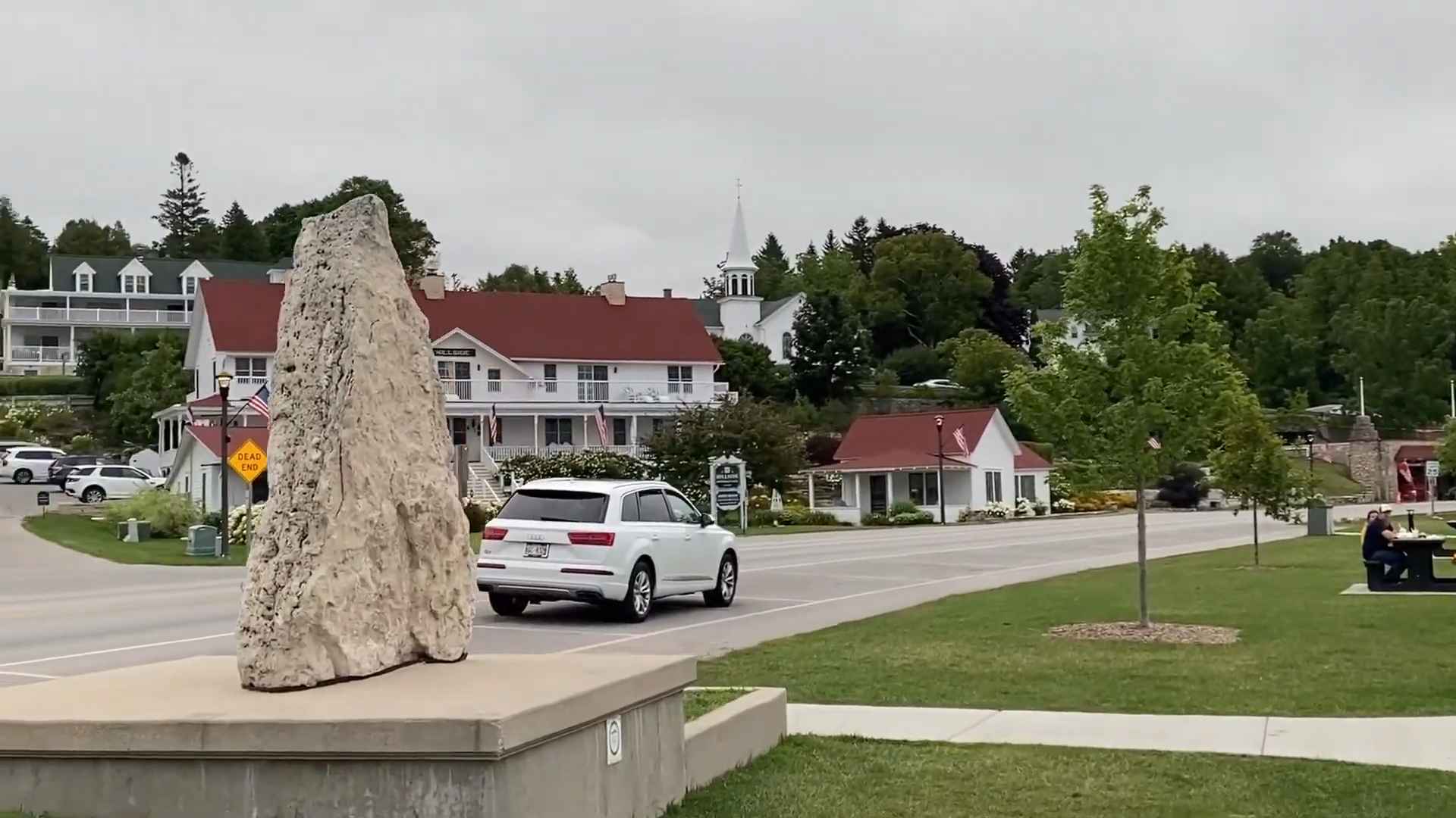 Large limestone monument in the foreground with a small-town street, red-roofed buildings, and a white church steeple in the background