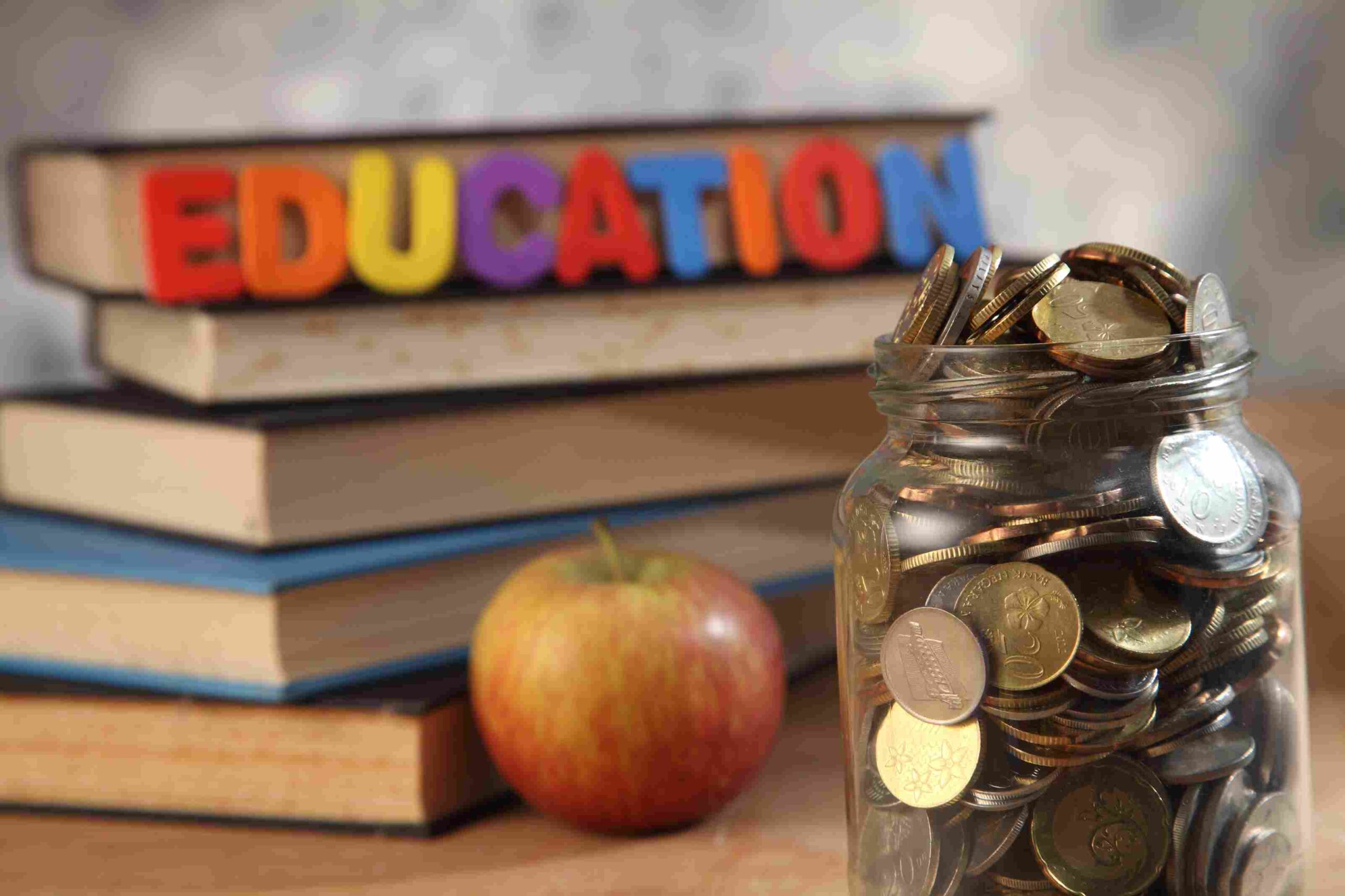 Jar filled with coins next to stacked books and colorful education letters with an apple
